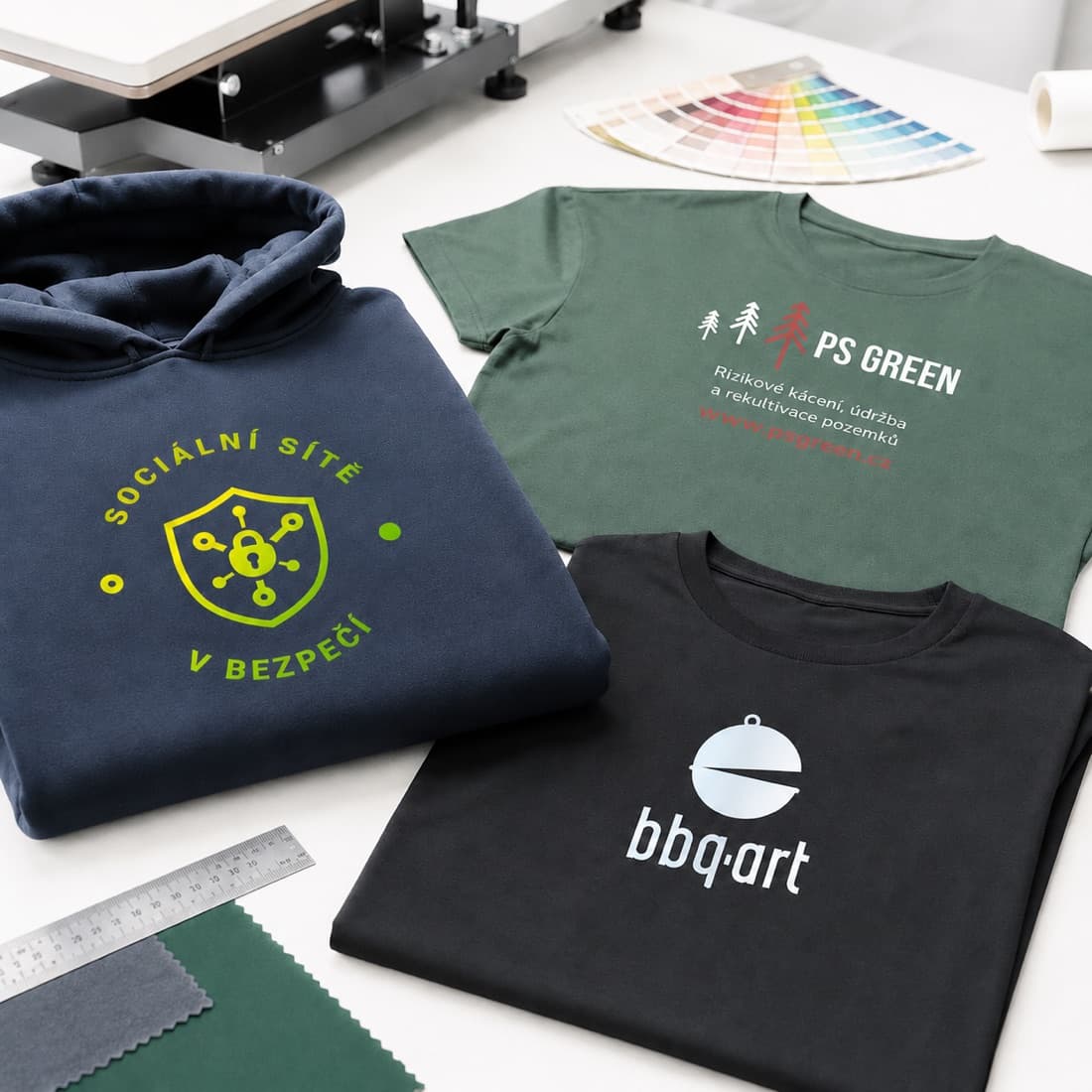 Potištěná trika a mikina s firemními logy na stole v dílně