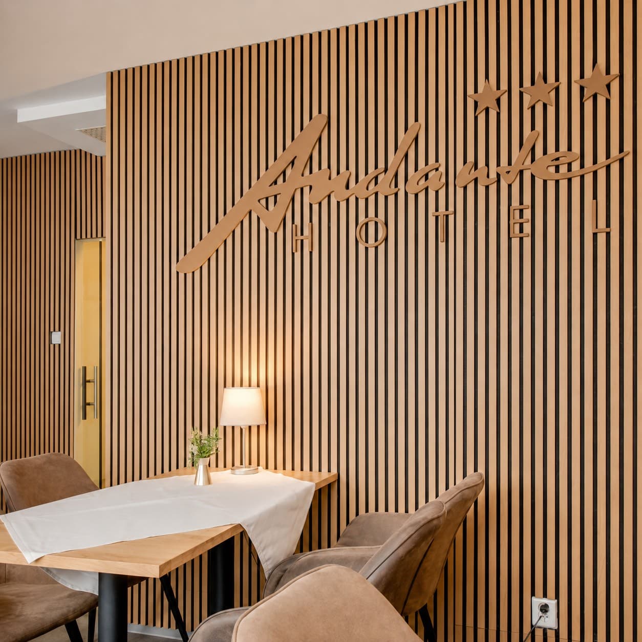 Prostorové logo Andante Hotel na dřevěné lamelové stěně kavárny