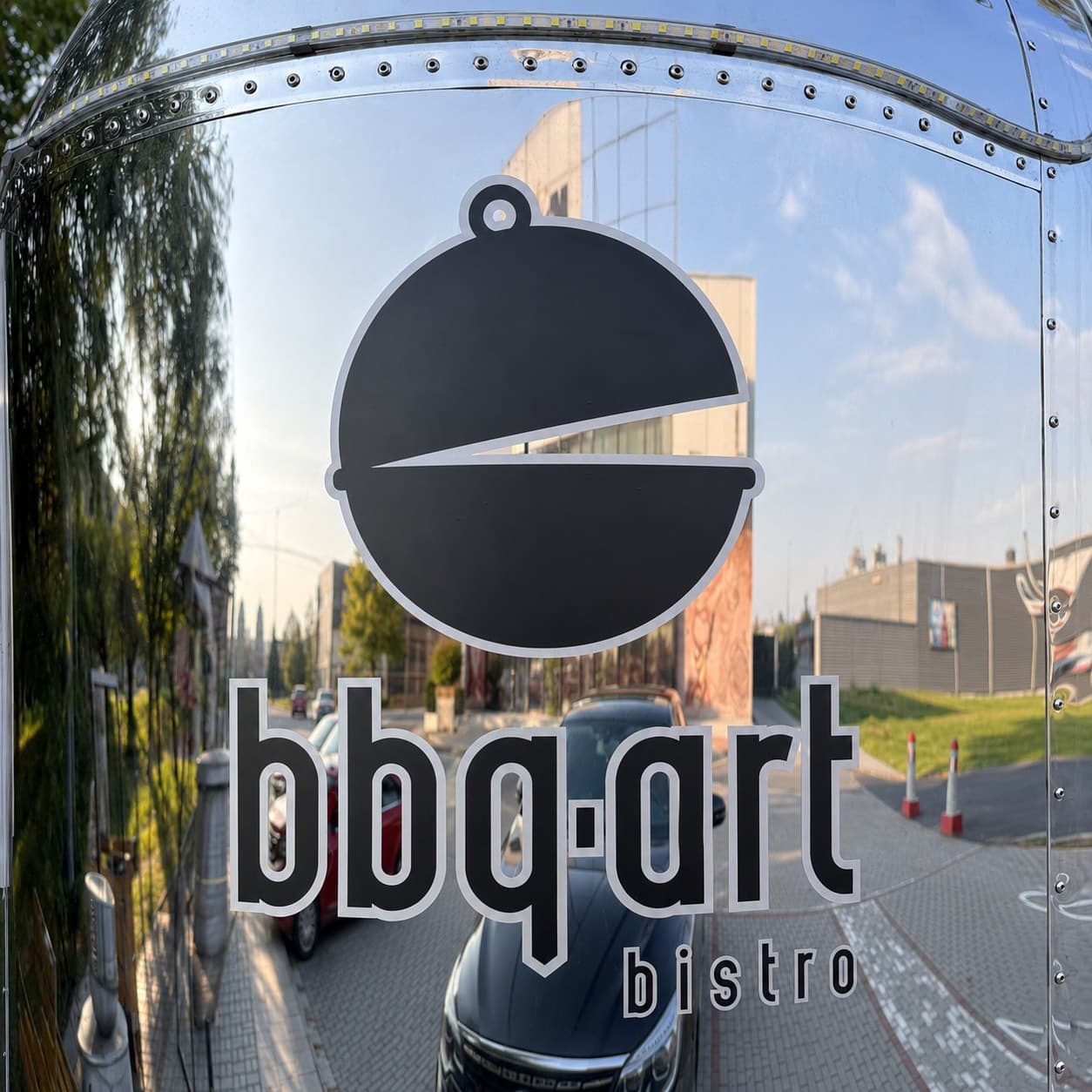 Detail černého loga BBQ Art s bílou konturou na zrcadlovém plechu