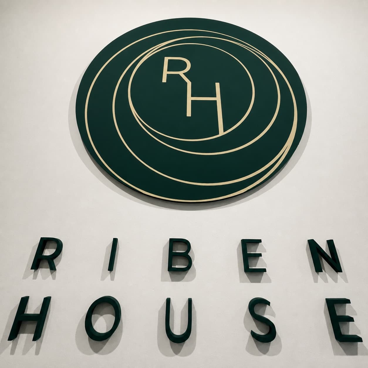 Zelené prostorové logo RIBEN HOUSE a 3D písmena na bílé stěně