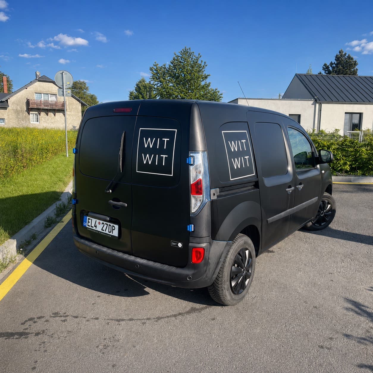 Zadní část černé dodávky s bílým logem WIT WIT z řezané fólie